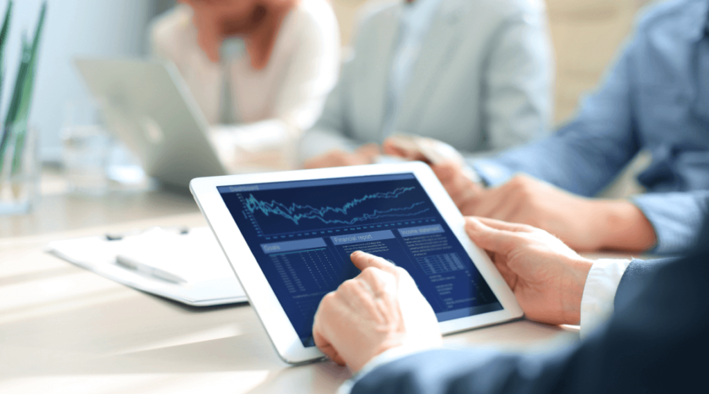 A business meeting, the main person is holding a tablet displaying stock market data and debt management solutions
