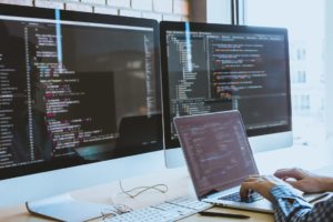 a photo of a programmer by a desk, in front of three displays