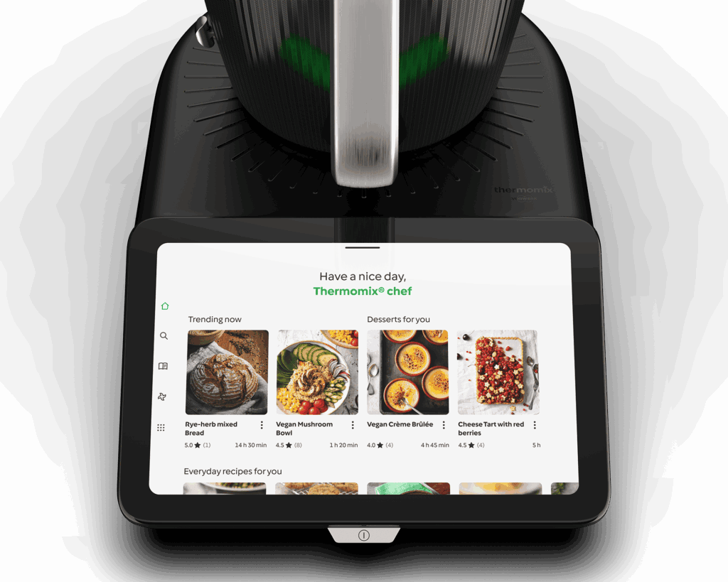 Close-up top view of Thermomix TM7 base unit with touchscreen display showing recipe home screen with trending and personalized recipe cards