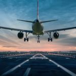 Commercial aircraft landing on a runway at sunset, viewed from the front with landing gear deployed.