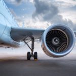 Close-up of a commercial aircraft engine and landing gear on the runway under a cloudy sky.
