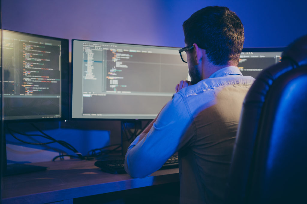 Rear back behind view portrait of nice focused skilled experienced guy thinking bug fixing debugging hardware software, trouble shooting data secure blockchain in dark room workplace station