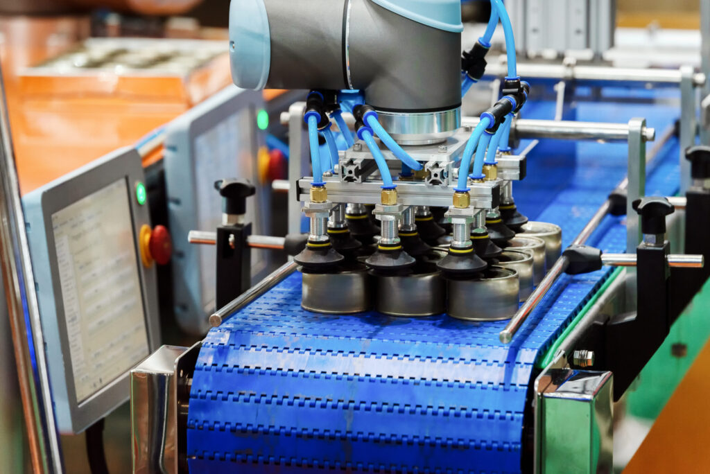 Robotic arm machine in factory is picking up canned food from a conveyor belt to deliver it to packaging, all working seamlessly thanks to food processing system integration.